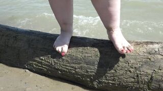 Bulky nude legs with red pedicure walk along the bank of the river, fetish.