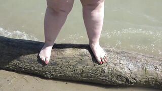 A obese woman with large feet walks along the shore.